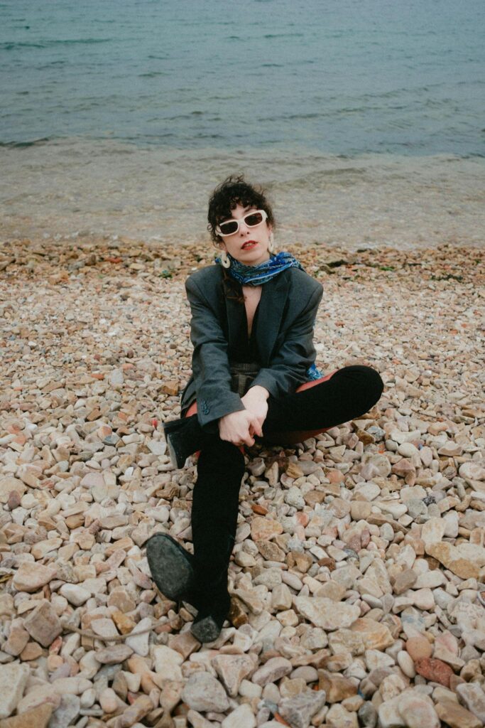 Stylish adult on rocky shore wearing sunglasses and scarf, by the sea.