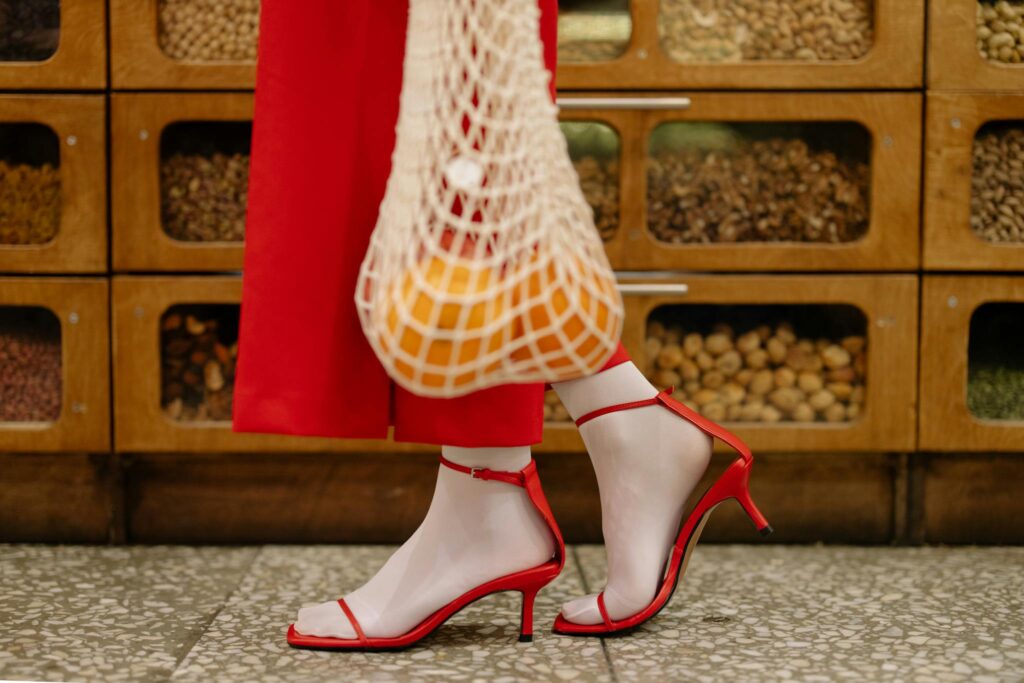 Stylish shopping scene with red heels and reusable net bag at grocery store.